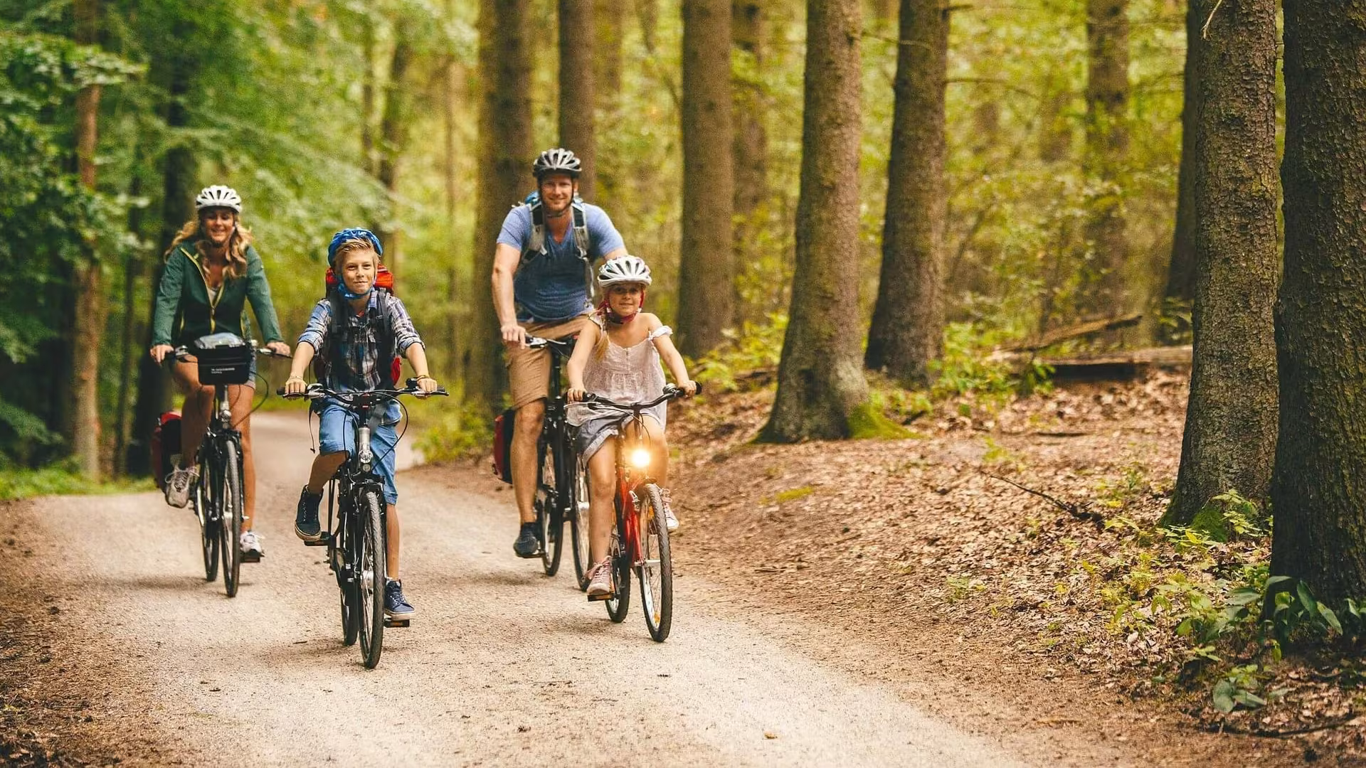 Familie mit zwei Kindern fährt mit Fahrrädern auf einem Waldweg