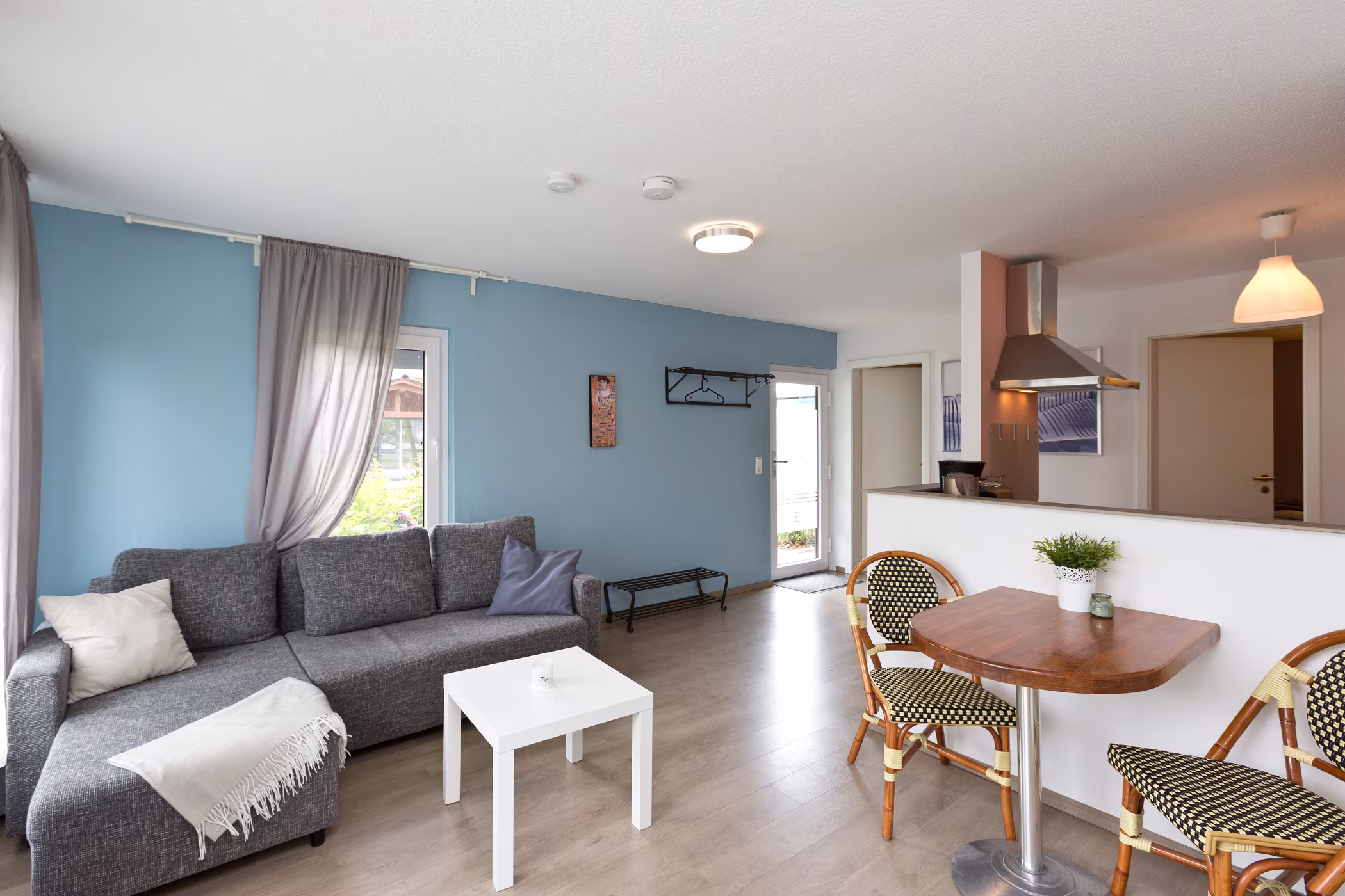 Heller Wohn- und Essbereich mit grauem Sofa, blauer Wand und offener Küche in der Ferienwohnung in Jabel